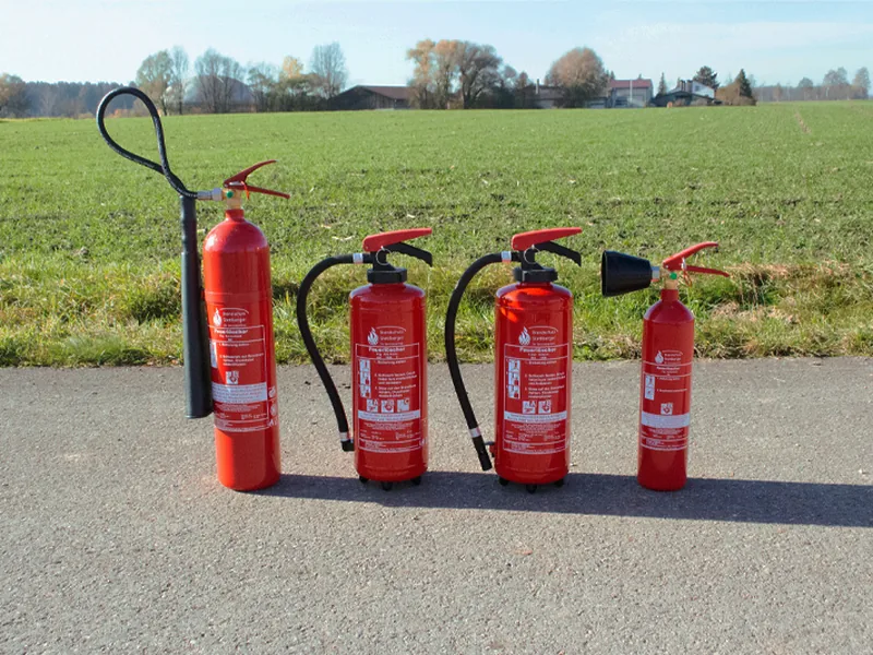 Vier Feuerlöscher unterschiedlicher Größe stehen nebeneinander auf einem Hof